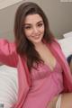 A woman in a pink robe sitting on a bed.