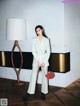 A woman in a white suit standing next to a lamp.