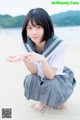 A young woman in a school uniform crouching on the beach.