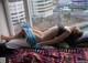 A naked woman laying on a bed in front of a window.