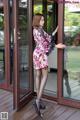 A woman in a floral dress is standing by a glass door.